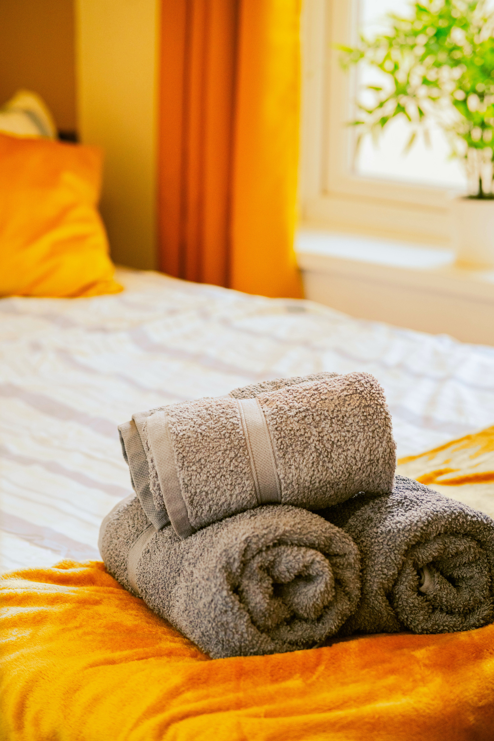 Rolled grey towels resting on softly folded white and mustard bed linen.