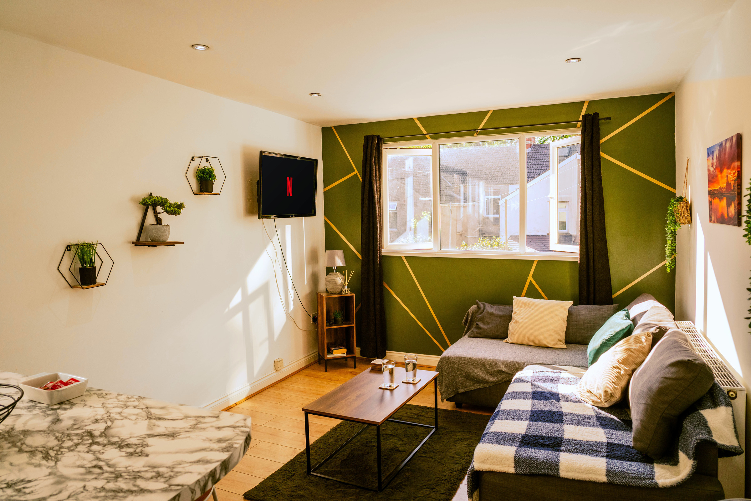 Wide view of the apartment lounge with a sofa, nesting tables and green geometric feature wall.