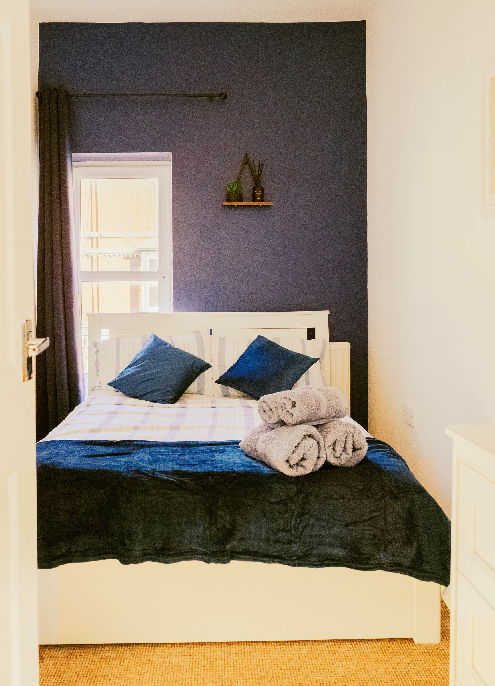 Double bed with navy bedding and rolled towels seen through the bedroom doorway.