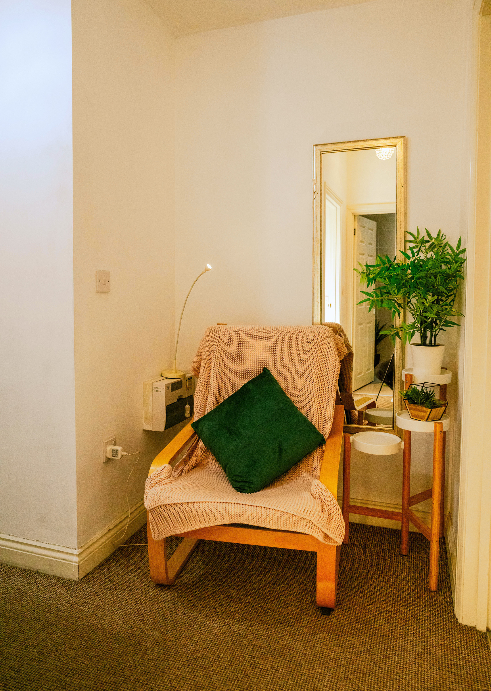 A softly lit reading chair with a green cushion and adjoining white side table.