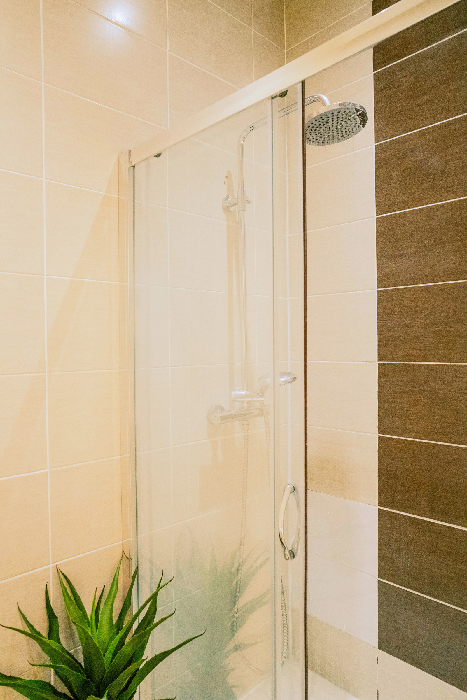 Glass shower enclosure and chrome shower fittings against white and grey bathroom tiles.
