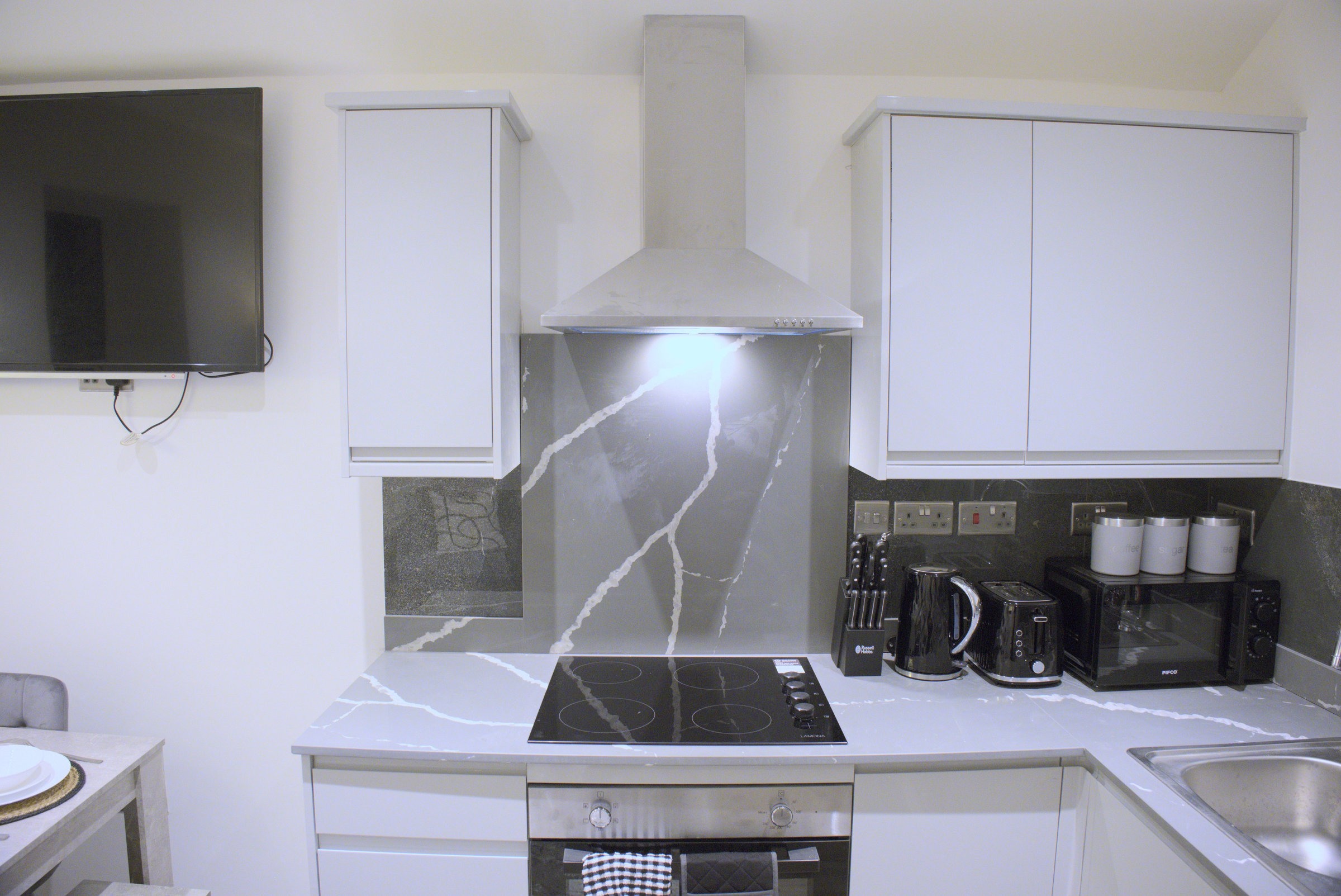 White kitchen cabinets with a marble-pattern splashback, hob and small appliances.