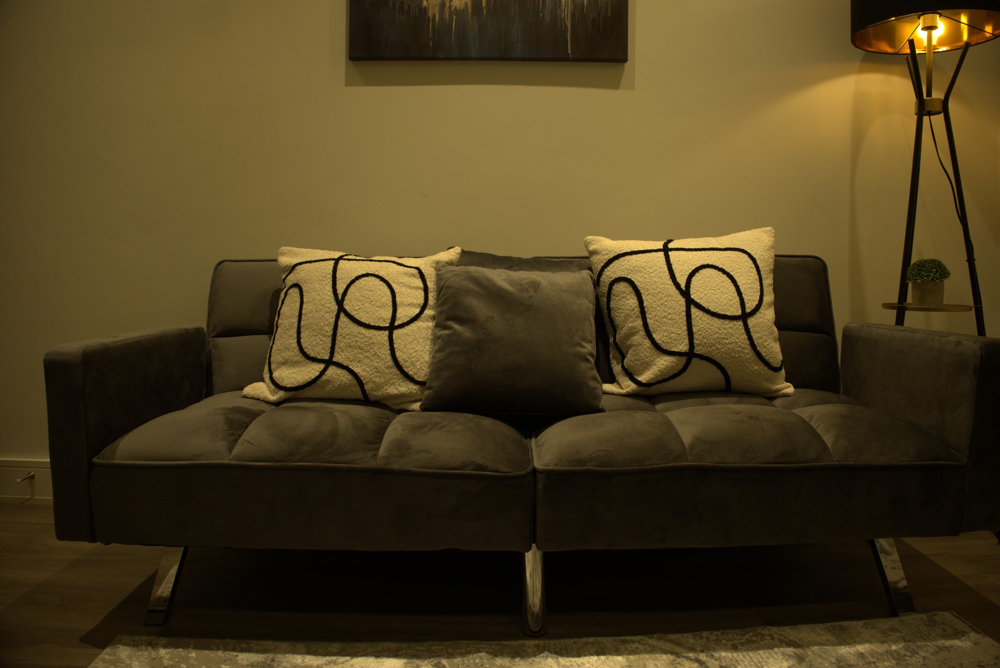 Before: Original camera photograph of a sofa, patterned cushions and a brass lamp before exposure and colour correction.