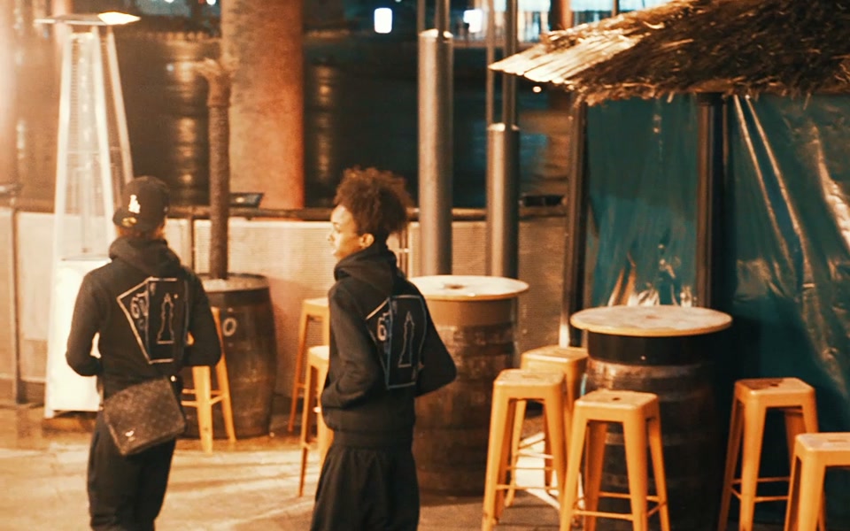 A genuine finished brand-film frame of two models walking through a warmly lit terrace.